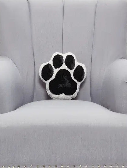 Hook and latch tufted black and white paw shaped pillow on a grey armchair